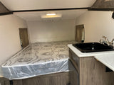 RV rental interior featuring a compact sleeping area with a mattress, a small kitchen sink, and overhead lighting.
