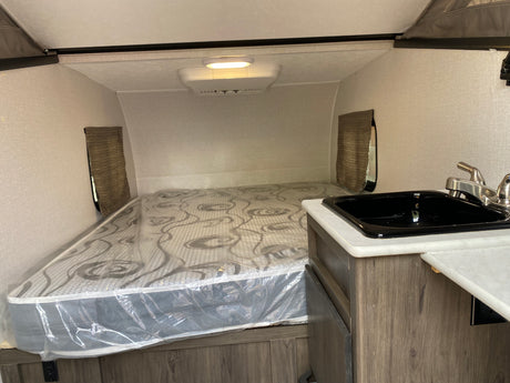 RV rental interior featuring a compact sleeping area with a mattress, a small kitchen sink, and overhead lighting.