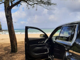 Black SUV, door open, on a scenic beach under a tree. Ocean waves beyond. Perfect trip, no RV rental needed.