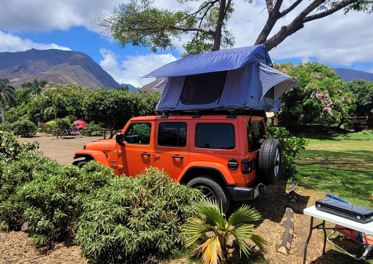 Orange Jeep with rooftop tent set up for an RV rental camping trip in lush mountain landscape. — photo 16