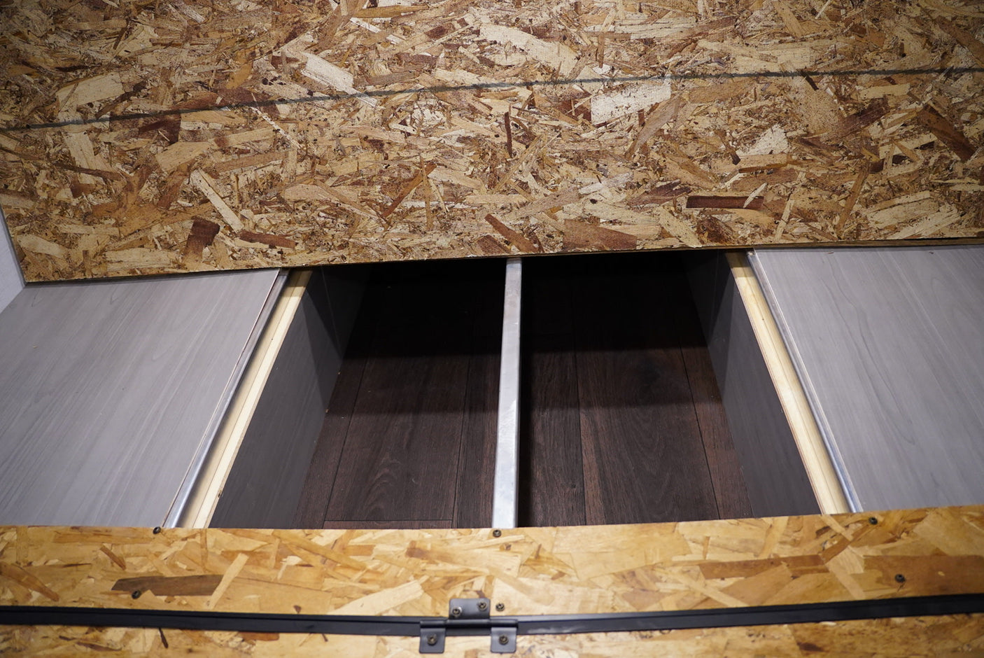 RV rental: Under-bed storage compartment revealed, featuring gray sliding doors, a metal divider, and OSB paneling.