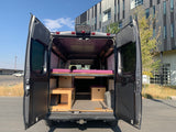 Discover this custom-built RV rental. Its open rear doors display a thoughtfully designed camper van interior with bed & storage.