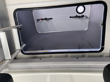 Inside an RV rental: Looking up into a spacious pop-top sleeping area with ladder access and integrated light.