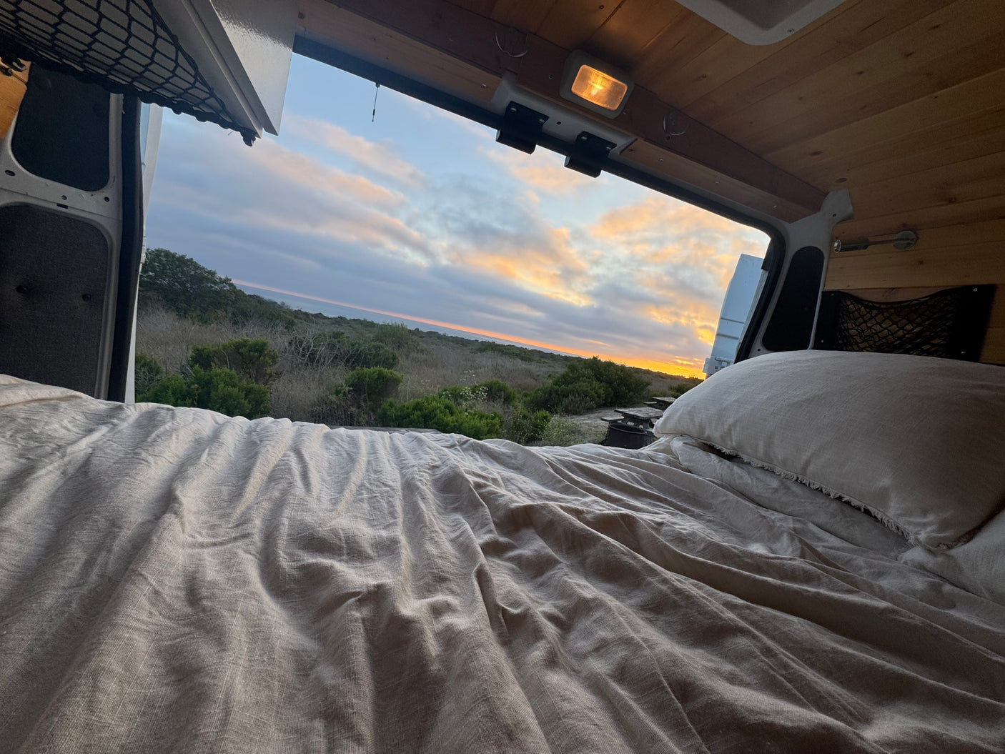 Relaxing in an RV rental campervan bed with a beautiful sunset view over a natural landscape and campsite.