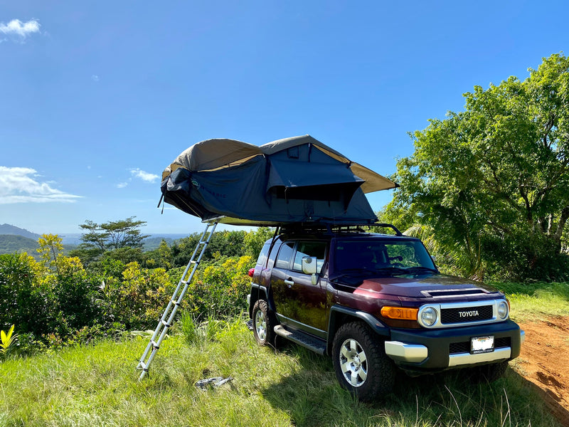 Dark red Toyota FJ Cruiser with a deployed rooftop tent on a grassy hill, overlooking scenic mountains and ocean. Ideal for an RV rental adventure. — photo 7