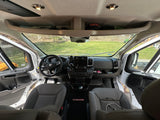 RV rental van interior: view of the modern dashboard, Ram steering wheel, gray seats, and overhead storage. Doors are open.