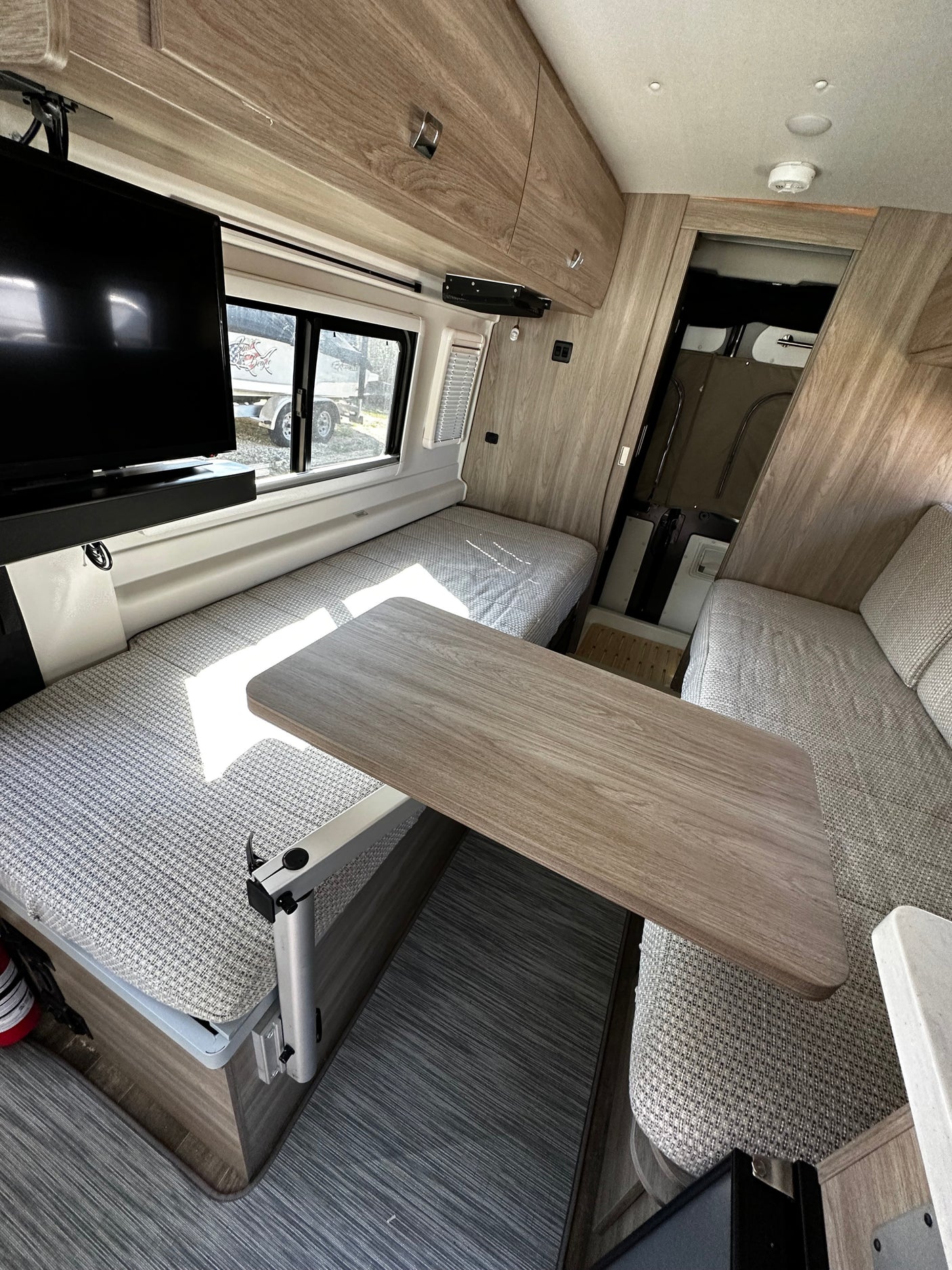 Inside a modern rv rental: a flexible dining area with a table, benches convertible to beds, overhead storage, and a TV.