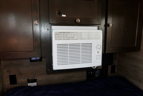 Compact AC unit in an RV rental, integrated into dark wood cabinetry above a bed.