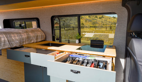 This RV rental interior showcases a modern kitchen, cozy bed, and smart, organized storage solutions for your travels.