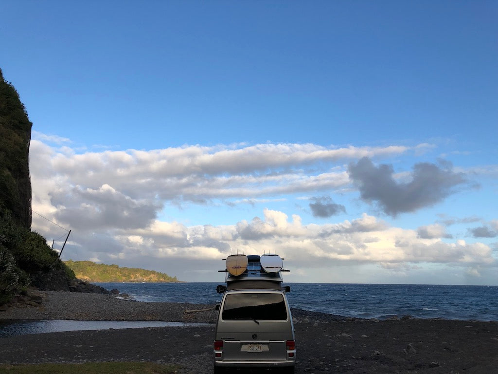 This rv rental camper van with surfboards enjoys a scenic ocean and beach view, nestled by a green cliff under a cloudy sky. — photo 7