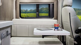 Inside a bright RV rental: a compact living space with table, tablet, mug, and glasses. Enjoy vineyard views through the window.