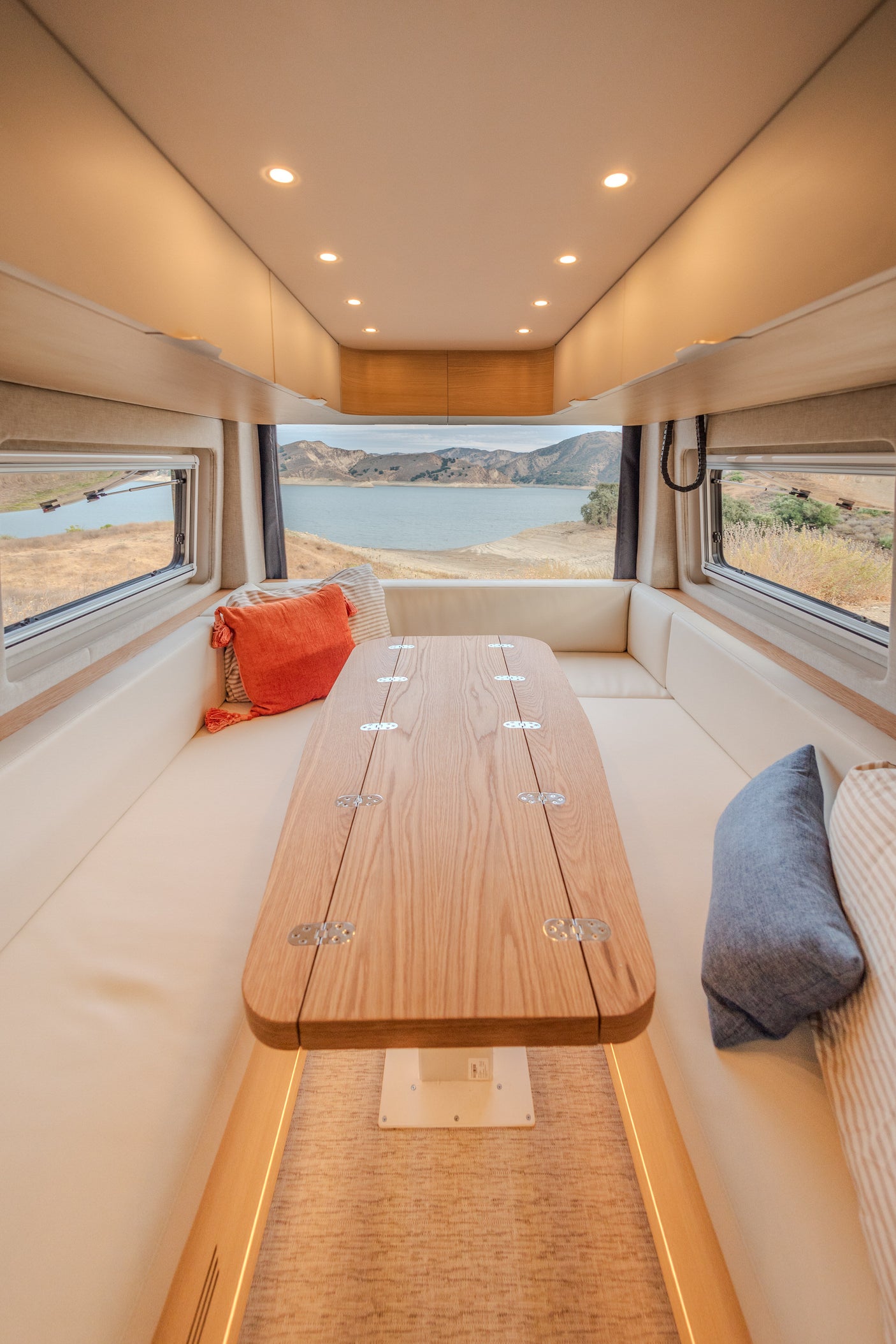 Inside a luxurious RV rental: a cozy dinette with a foldable table and panoramic lake views for your next adventure.