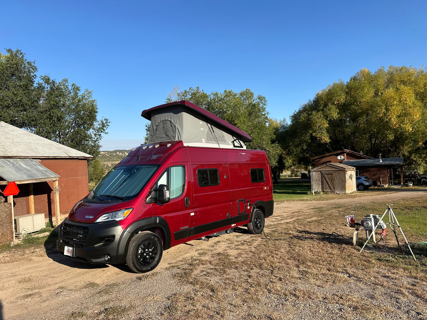 Red Winnebago Solis camper van with pop-top extended, parked in a rural setting, perfect for your RV rental.