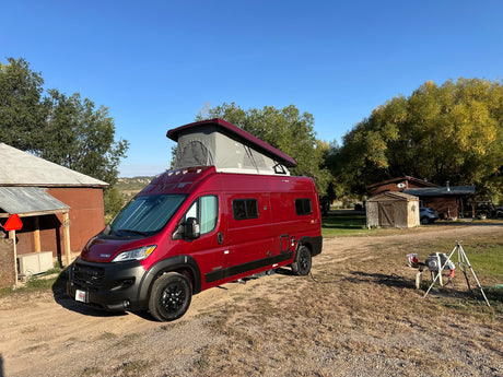 Red Winnebago Solis camper van with pop-top extended, parked in a rural setting, perfect for your RV rental.