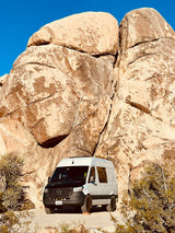 RV rental: White camper van parked by immense boulders and desert plants under clear blue sky, ideal for off-grid adventures.