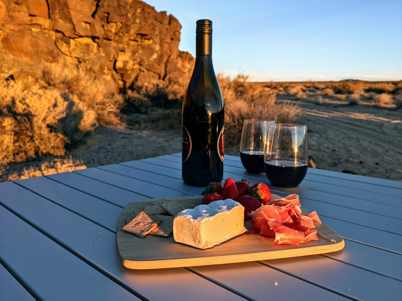 RV rental escape: Red wine, cheese, strawberries, prosciutto, and crackers on a table, sunset desert backdrop.