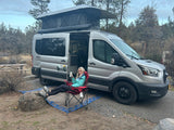 Woman relaxing by a ModVans pop-top rv rental van, perfect for camping and outdoor adventures.
