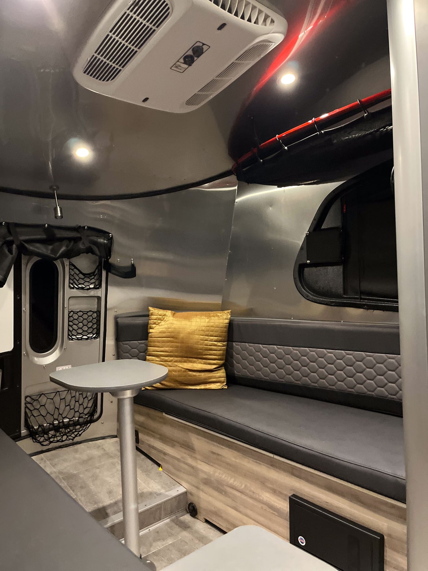 RV rental interior: A modern living space with curved aluminum walls, a grey bench seat, golden pillow, and overhead AC unit. — photo 6