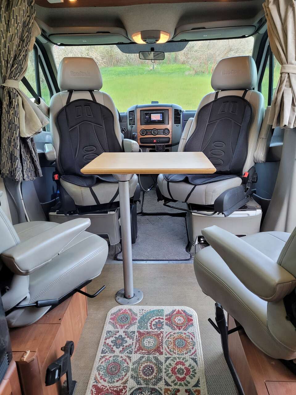  and a large window view of a vibrant green landscape.|Two blue sleeping bags laid out in this cozy RV rental's camper van interior — photo 3