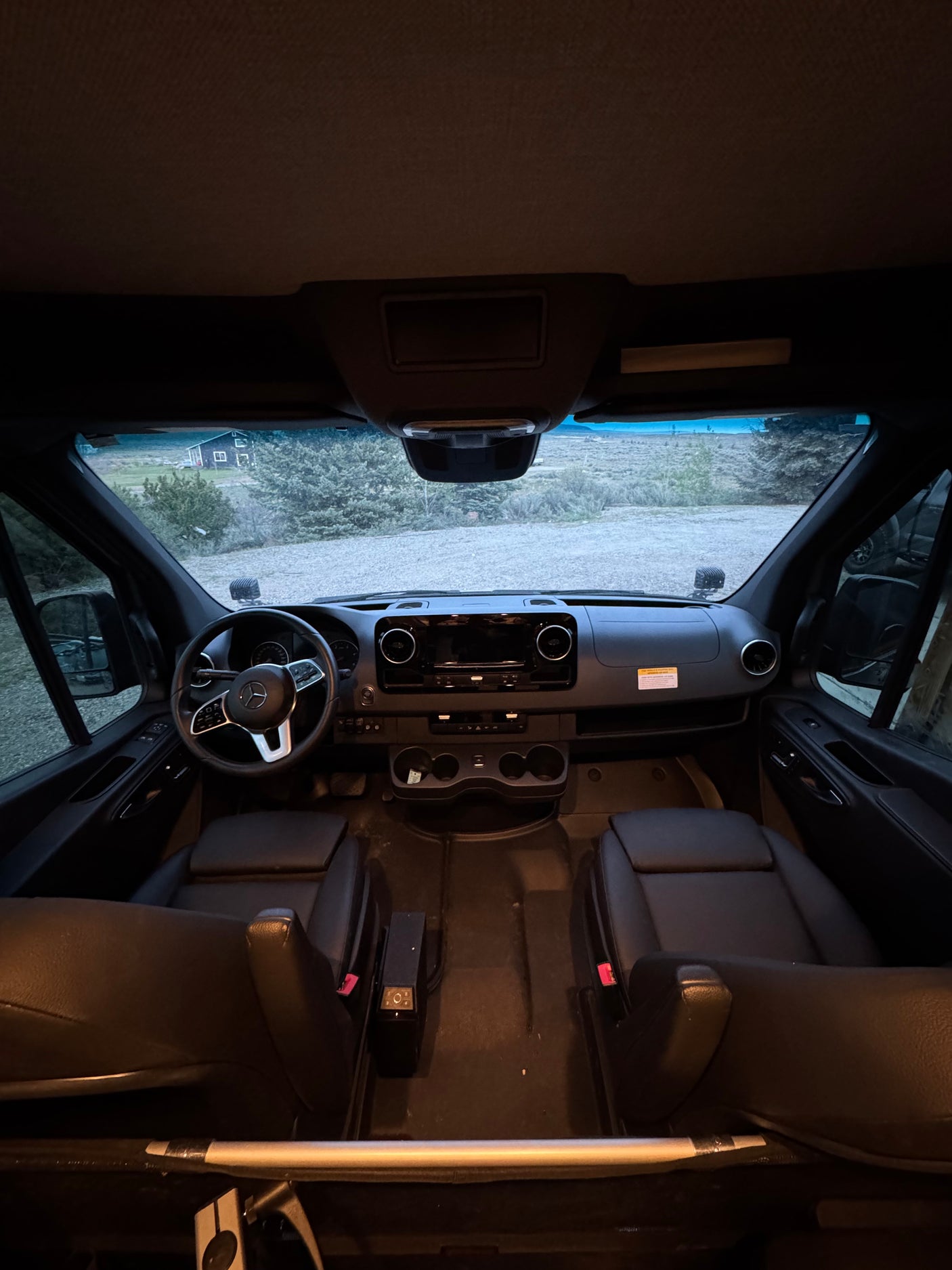 RV rental van interior: dashboard, steering wheel, front seats. Outside, a distant house in a natural landscape.
