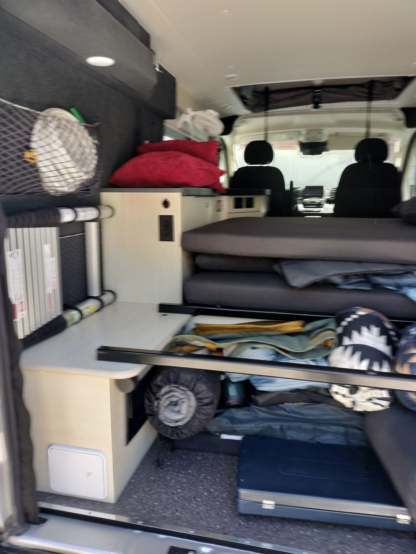 Explore this RV rental's cozy camper van interior: comfortable bed, overhead bins, and smart storage solutions.