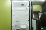 Compact RV rental bathroom with a white toilet and shower area in a camper van, featuring a bright green door.