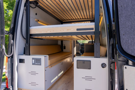 Modern rv rental camper van interior featuring comfortable bunk beds, tan cushions, and a control panel.