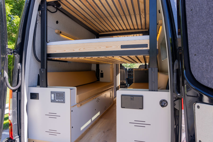 Modern rv rental camper van interior featuring comfortable bunk beds, tan cushions, and a control panel.