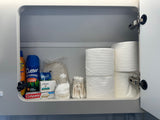 Inside an RV rental cabinet: organized shelf with travel toiletries like bug spray, toothpaste, soap, & toilet paper.