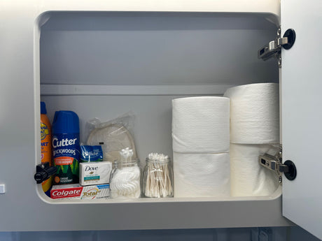 Inside an RV rental cabinet: organized shelf with travel toiletries like bug spray, toothpaste, soap, & toilet paper.