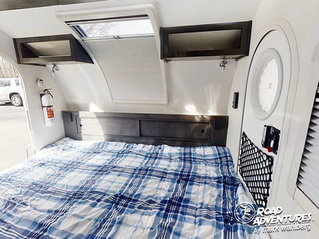Inside an RV rental: a comfy bed with plaid comforter, storage, skylight, and fire extinguisher.