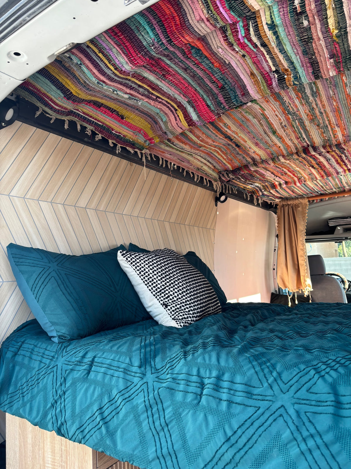 Cozy RV rental bed with a vibrant rag rug ceiling, teal bedding, and patterned wood walls, perfect for campervan adventures. — photo 7
