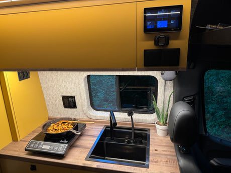 Sleek camper van kitchen with induction cooktop, sink, and power monitor. Ideal for rv rental journeys.