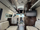 Looking inside a luxury RV rental. This spacious camper van interior features cream seating, wood floors, a compact kitchen, and TVs.