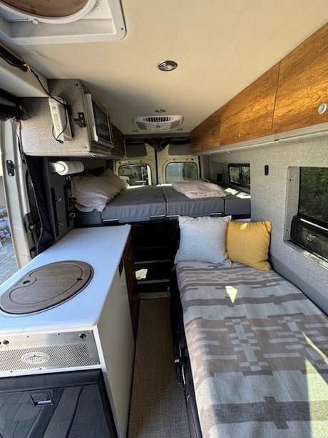 Inside an RV rental: a cozy camper van interior with a galley, elevated rear bed, and side bench/bed.