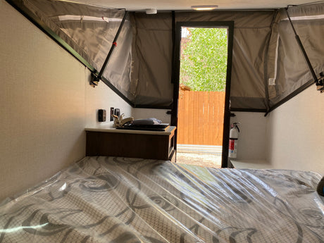 Inside an RV rental pop-up camper: bed with plastic, compact sink, and open door to the outdoors.