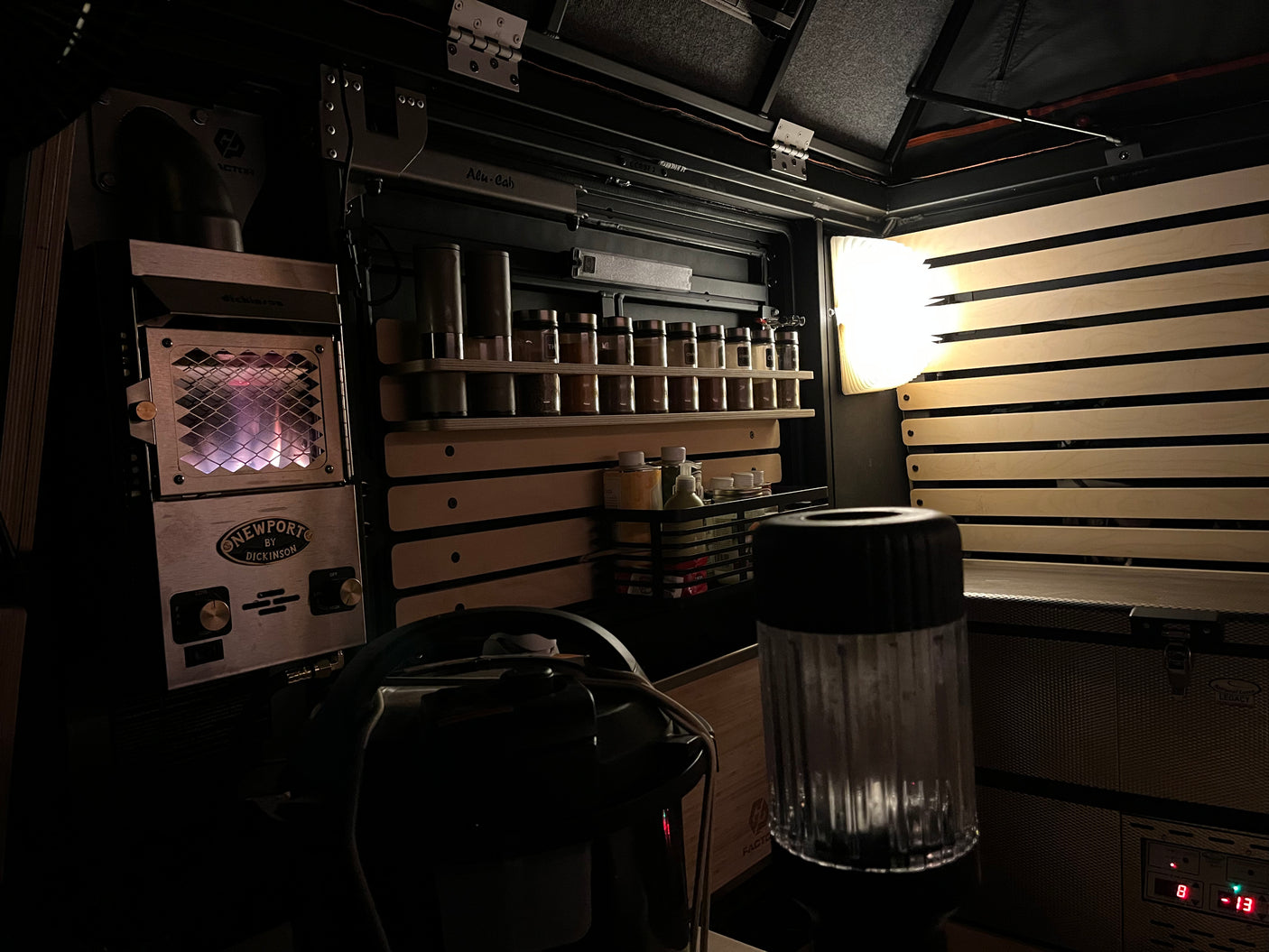 View of an RV rental interior at night, showing a glowing Dickinson heater, organized spice rack, and Alu-Cab storage.