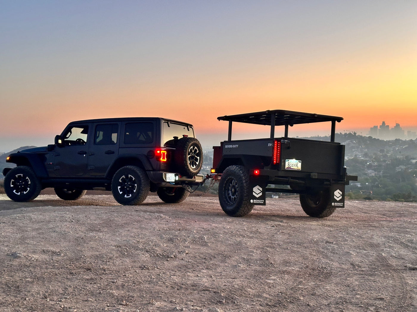 A dark Jeep tows an off-road utility trailer at sunset, overlooking a city. Ideal setup for an RV rental adventure. — photo 8