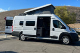 White Winnebago Solis rv rental with extended pop-top and open side/rear doors, showcasing its interior.