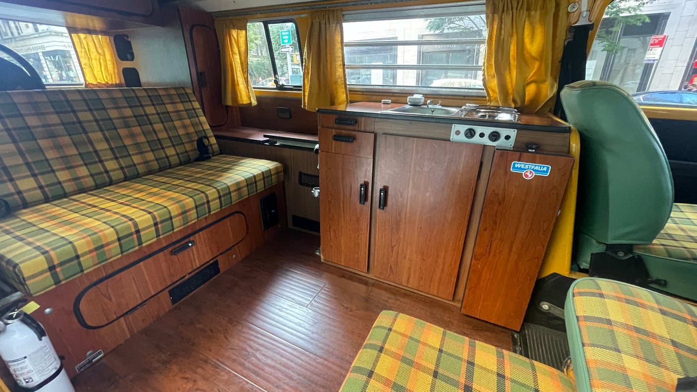 A cozy vintage RV rental interior with plaid seating, wooden cabinets, and a compact kitchenette.