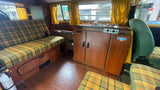 A cozy vintage RV rental interior with plaid seating, wooden cabinets, and a compact kitchenette.