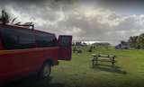 Enjoy RV rental camping by the ocean. A red van and other RVs are parked on green grass with a picnic table.