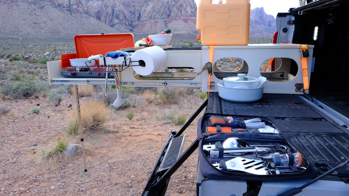 This RV rental outdoor kitchen, with a stove and supplies, extends from a truck bed amidst desert mountains for convenient camping meals. — photo 15