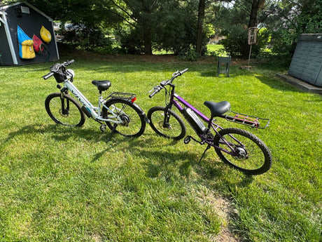Two electric bikes on a sunny green lawn by a shed, perfect for outdoor fun or an RV rental adventure.