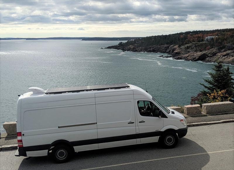 White RV rental van with solar panels on a scenic coastal road overlooking a vast ocean. — photo 15