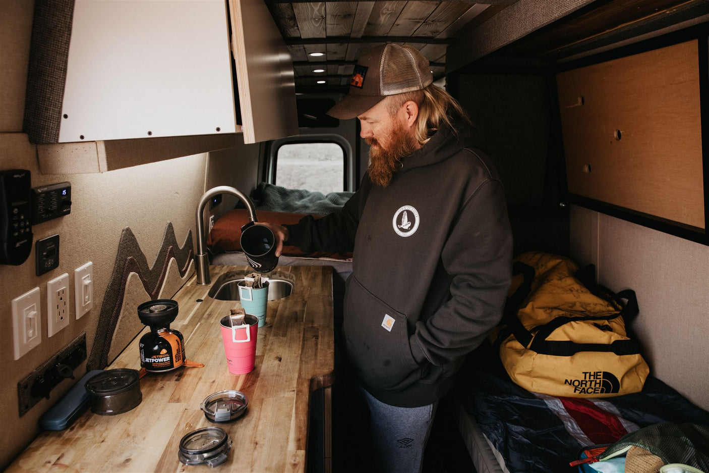 An RV rental's compact kitchen. A man makes coffee in his camper van, ready for the open road.
