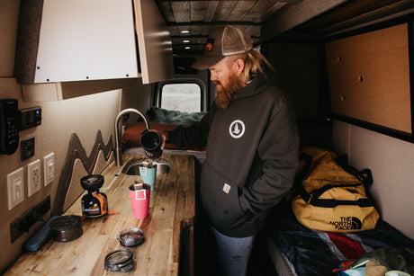 An RV rental's compact kitchen. A man makes coffee in his camper van, ready for the open road.