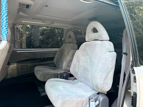 Spacious rear seats with unique headrests and dual sunroofs inside this RV rental van, offering a bright, airy feel.