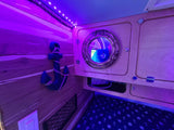 Cozy RV rental interior: purple-lit, nautical decor with porthole mirror, anchor, and patterned bunk bedding.