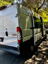 White Ram ProMaster van, configured for RV rental, with its rear and side doors open. Parked outdoors, dappled sunlight on the vehicle and ground.